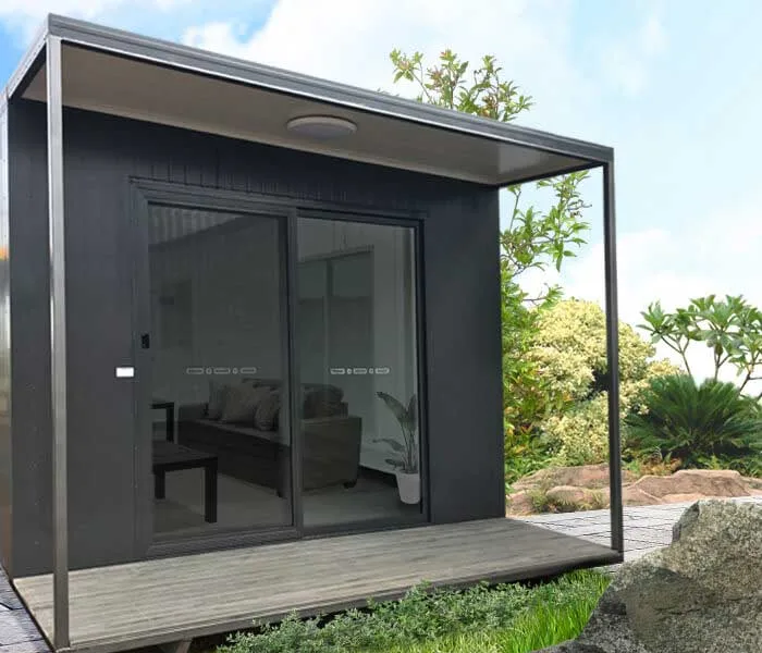 Charcoal portable studio building with a full-width sliding glass door opening onto a timber deck, set in a landscaped garden