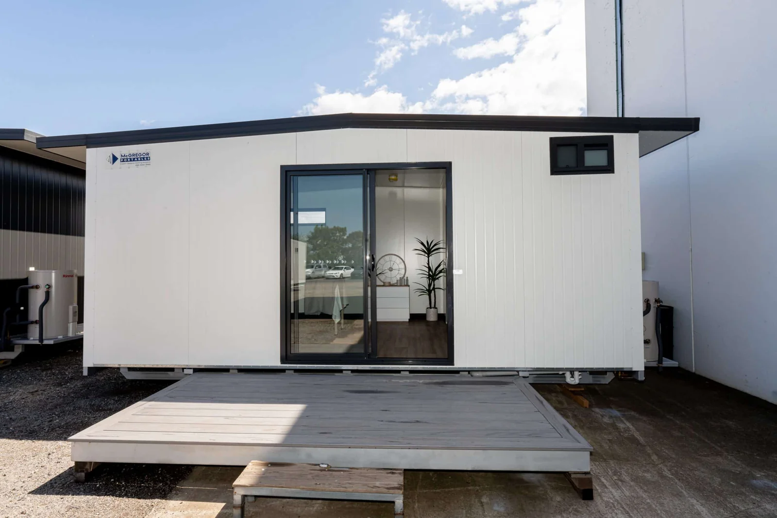 Temporary studio unit with a dark sliding glass door and a timber deck in front, standing under a shed roof.
