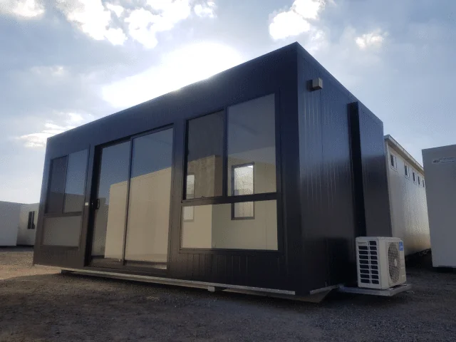 Charcoal sales office with full-height glazing and a glass entry door, on a gravel yard.