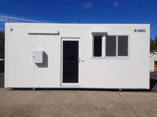 White gatehouse with a single door, a security-screened window and an electrical box mounted on the front wall.