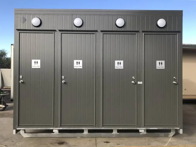 Grey unisex toilet block with four separate signed doors and four round vents along the roofline.