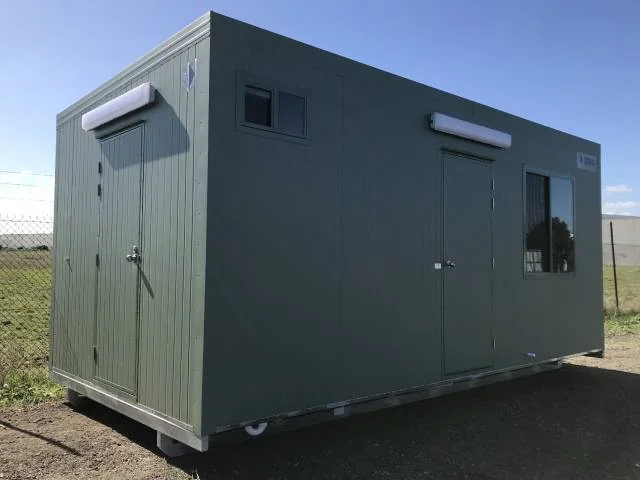 Olive-green eco lunchroom with an awning-shaded window and a door on the near end, standing on gravel.