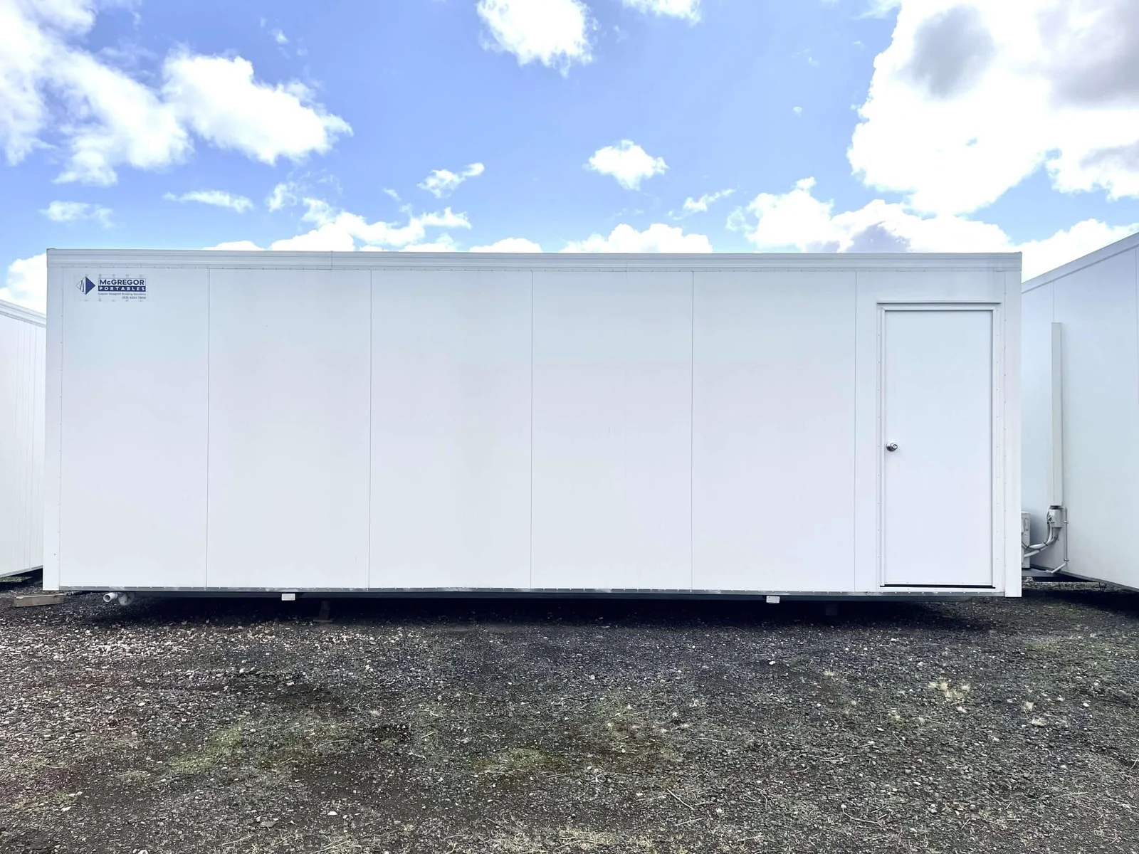 Long white site office with blank side cladding and a single door at the far end.