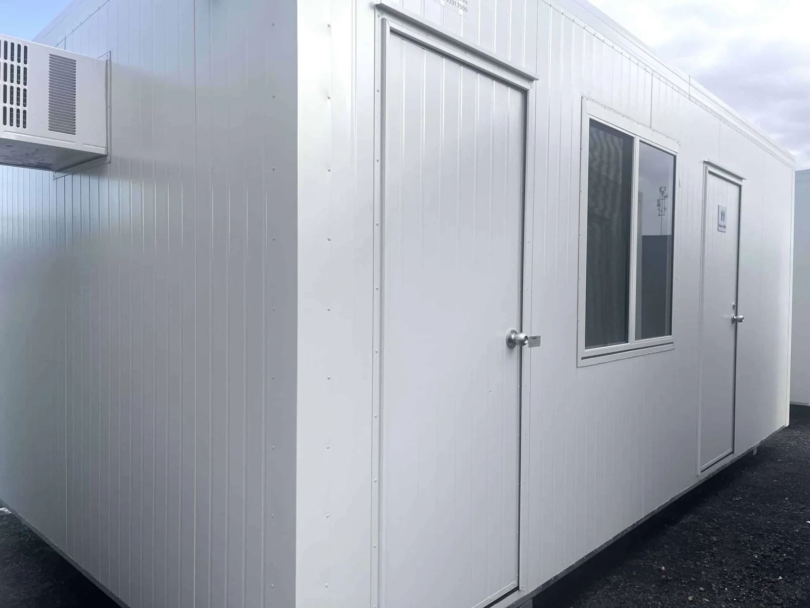 White lunchroom seen along its side, with a wall-mounted air conditioner, a door and a security-screened window.