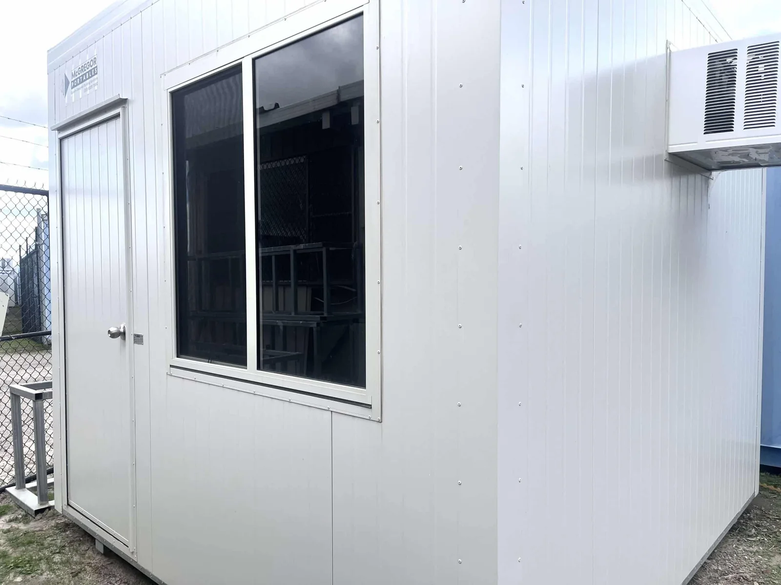 White lunchroom with a door, a large window and a wall-mounted air conditioner across the front.