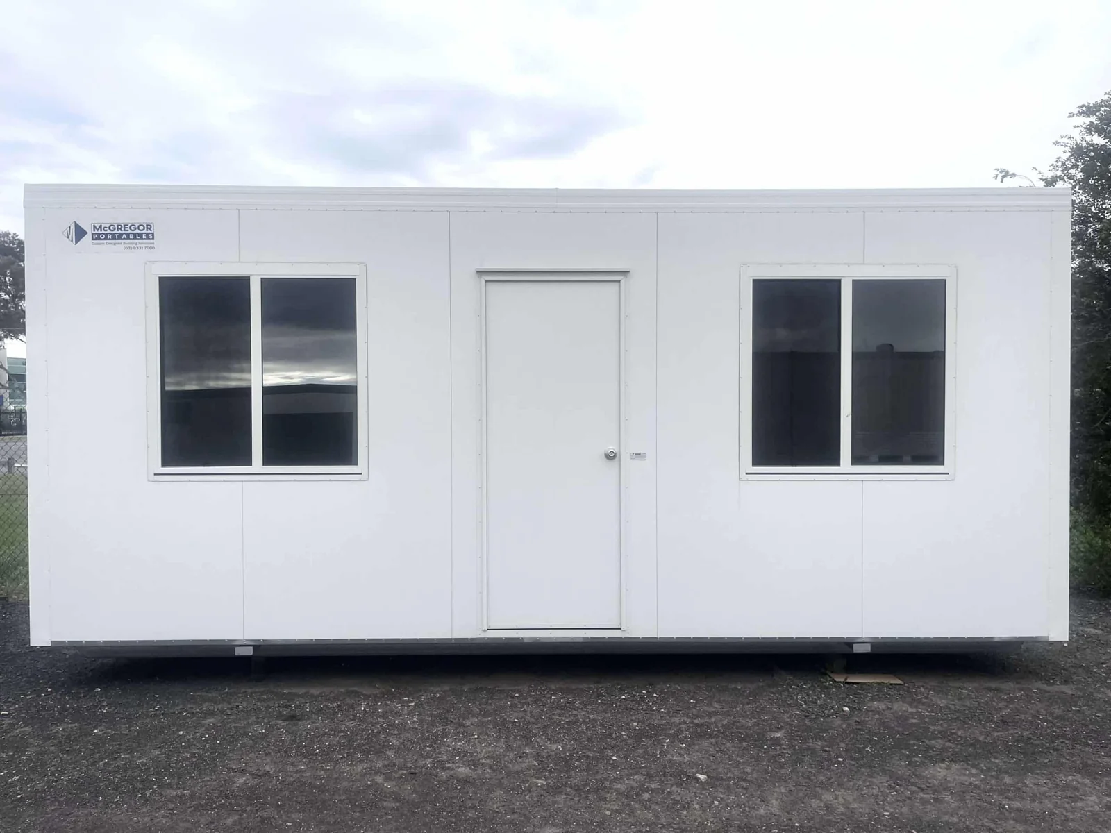 White site office with a central door set between two large windows, on a gravel yard.