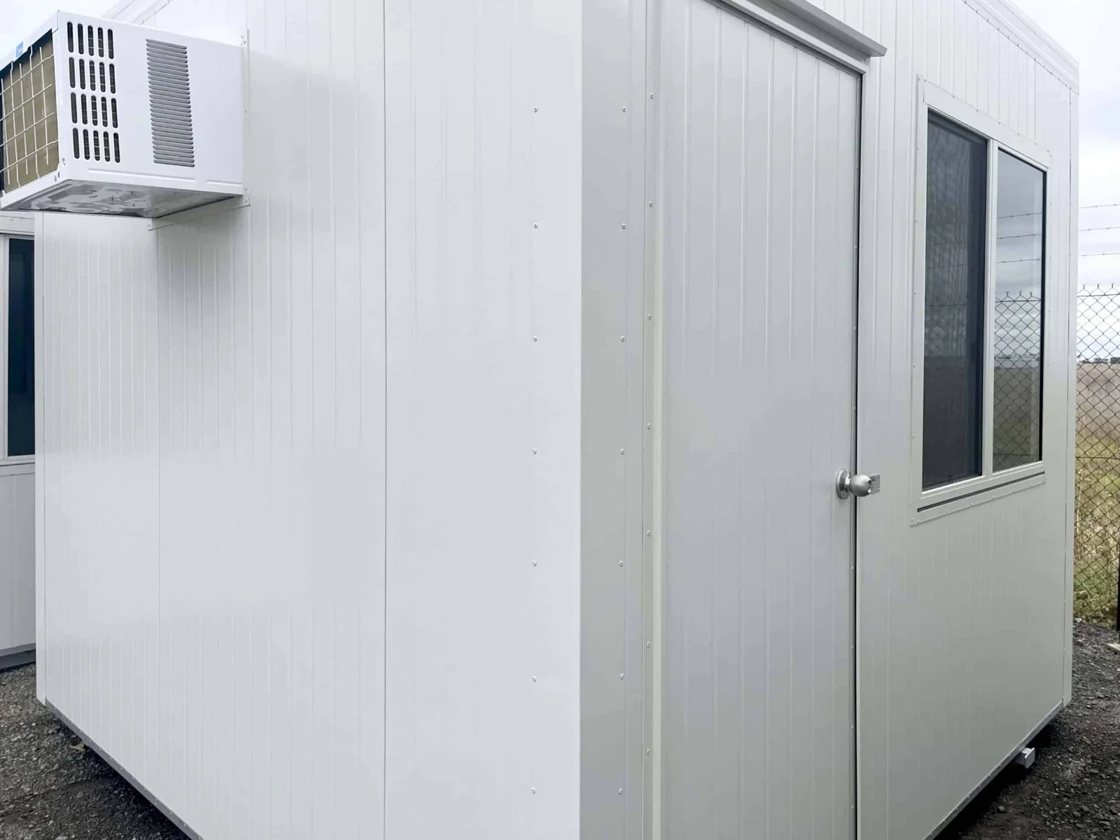 White site office seen from the corner, with a wall-mounted air conditioner and one window.