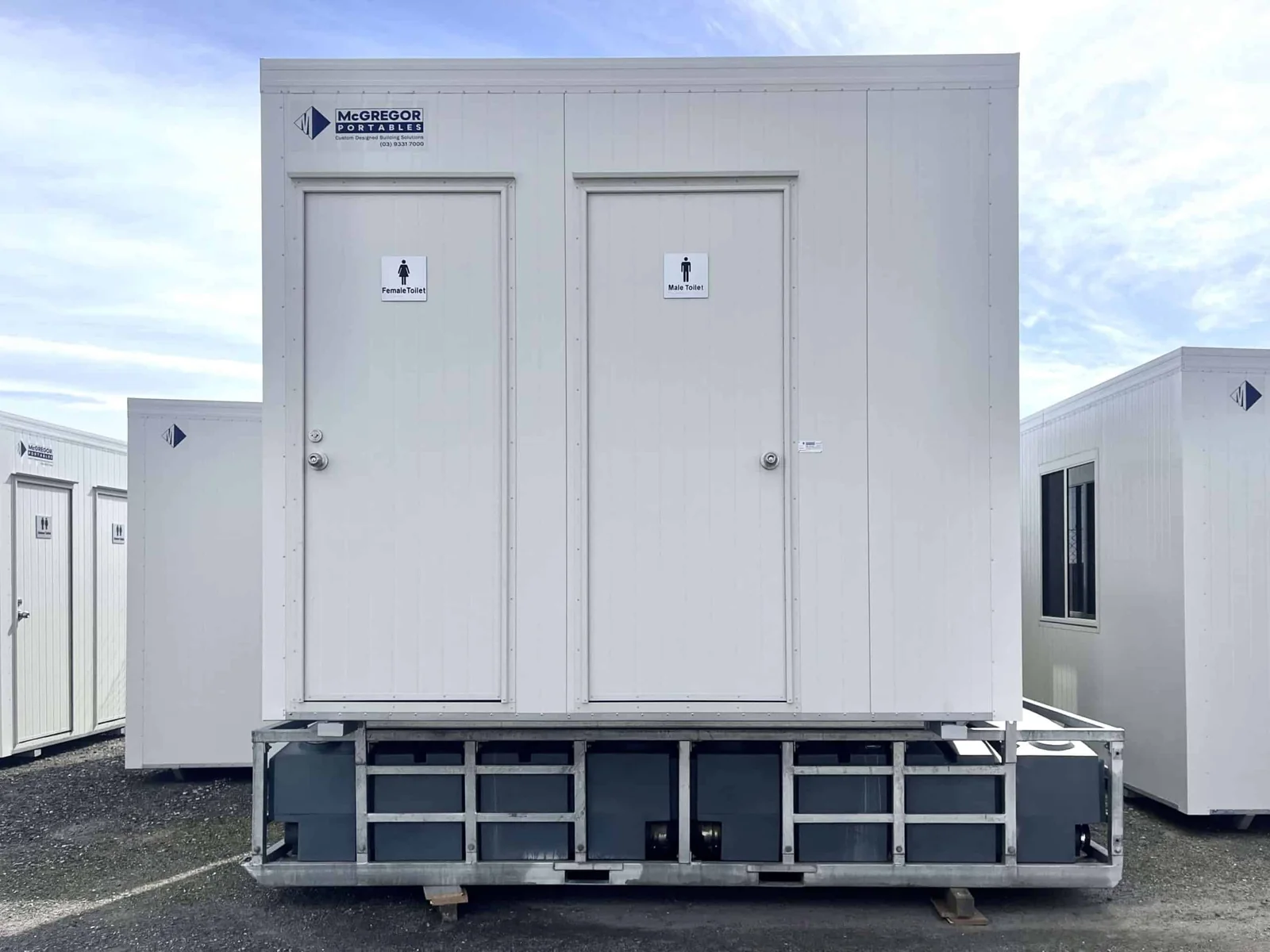 White male and female toilet block with two signed doors, mounted on a steel transport frame.