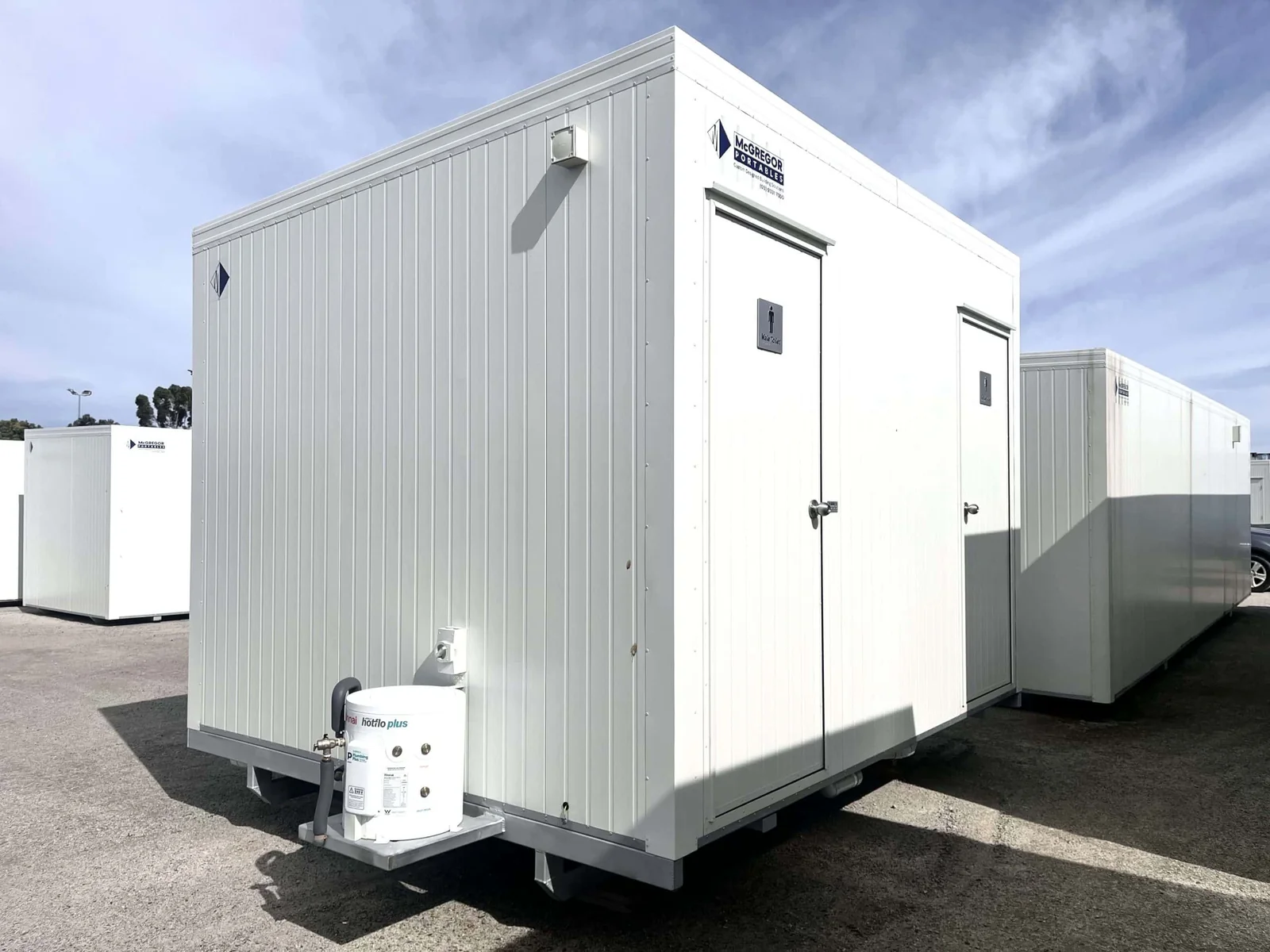 White toilet block with signed doors along the front and a small pump unit at the base.