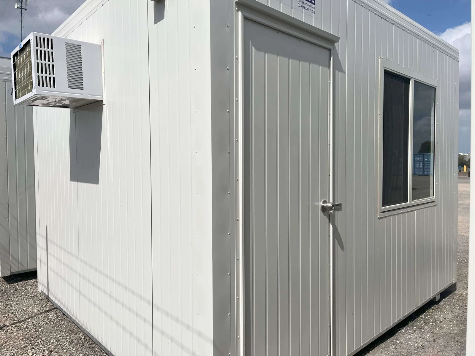 White site office seen from the corner, with a wall-mounted air conditioner, a door and a window.