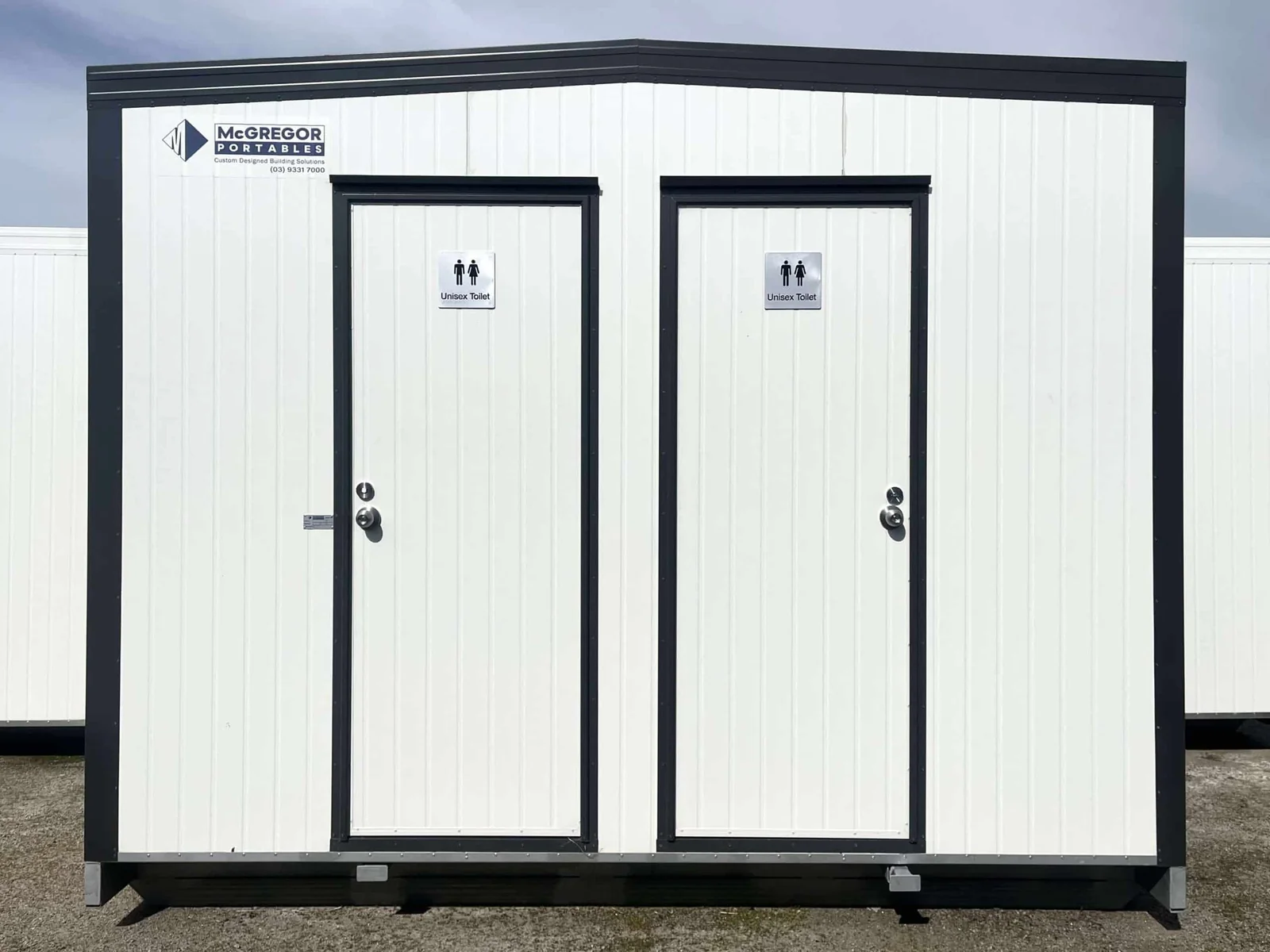White twin toilet unit with two signed doors, framed in dark trim and mounted on a dark base.