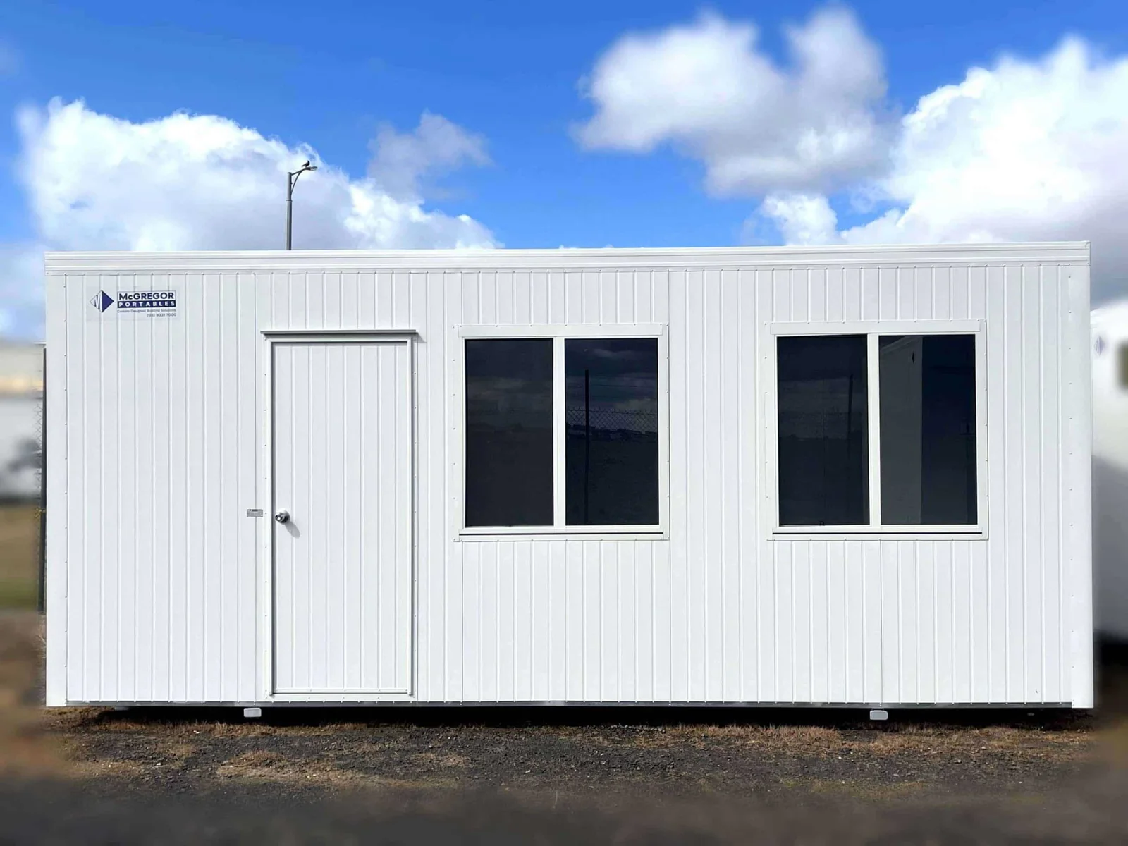 White site office with a door at one end and two windows, on a gravel yard.