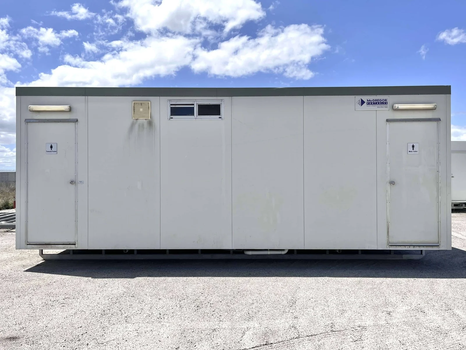 Secondhand toilet block in weathered grey, with a signed door at each end and vents along the roofline.