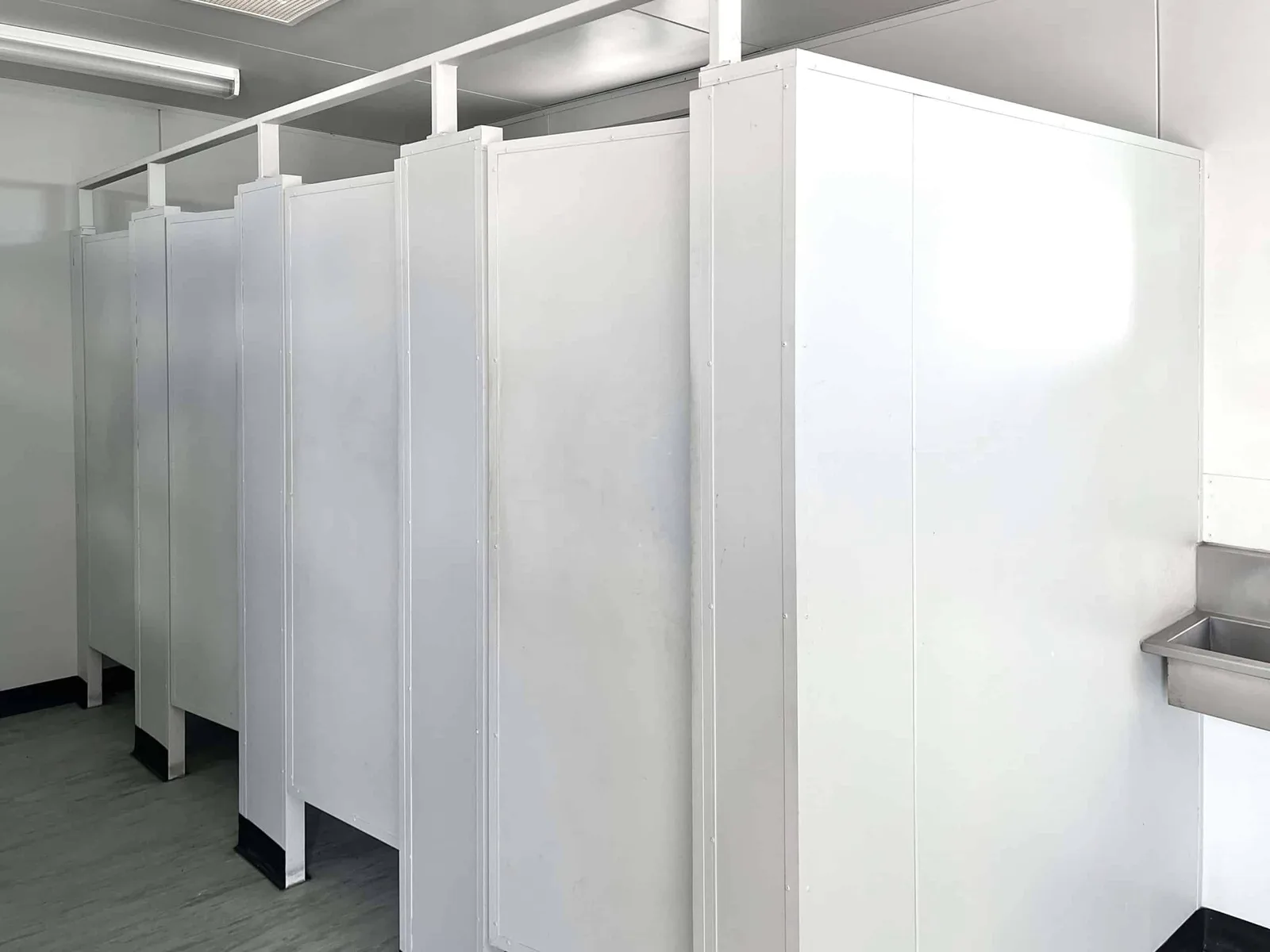 Row of toilet cubicles inside a portable ablution block, with a sink visible at the end of the corridor